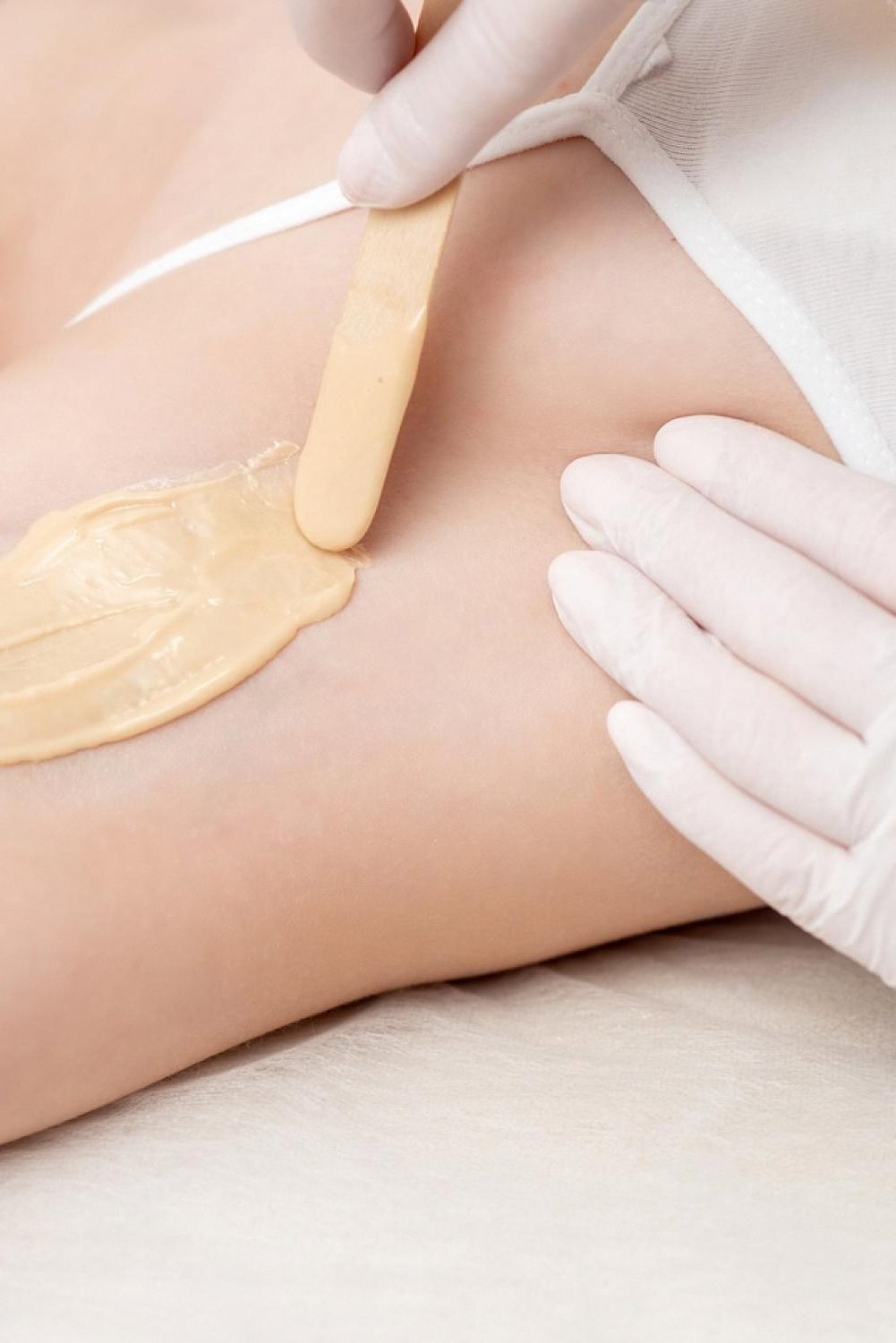 Warm wax being applied to a client's underarm with a wooden spatula in a salon
